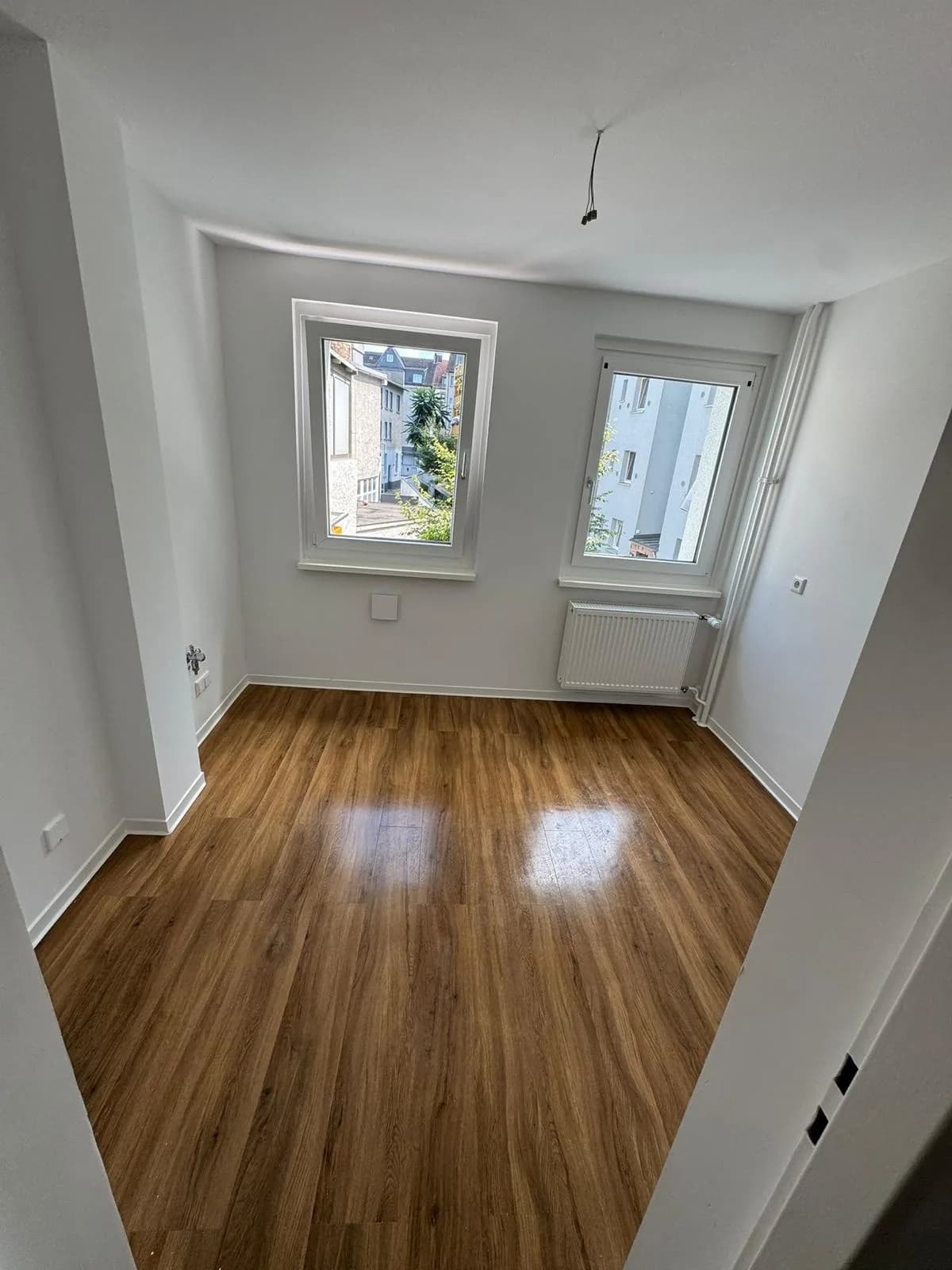 Sanierter Wohnraum mit neuem Holzboden, erneuerten Fenstern und neuem Heizkörper